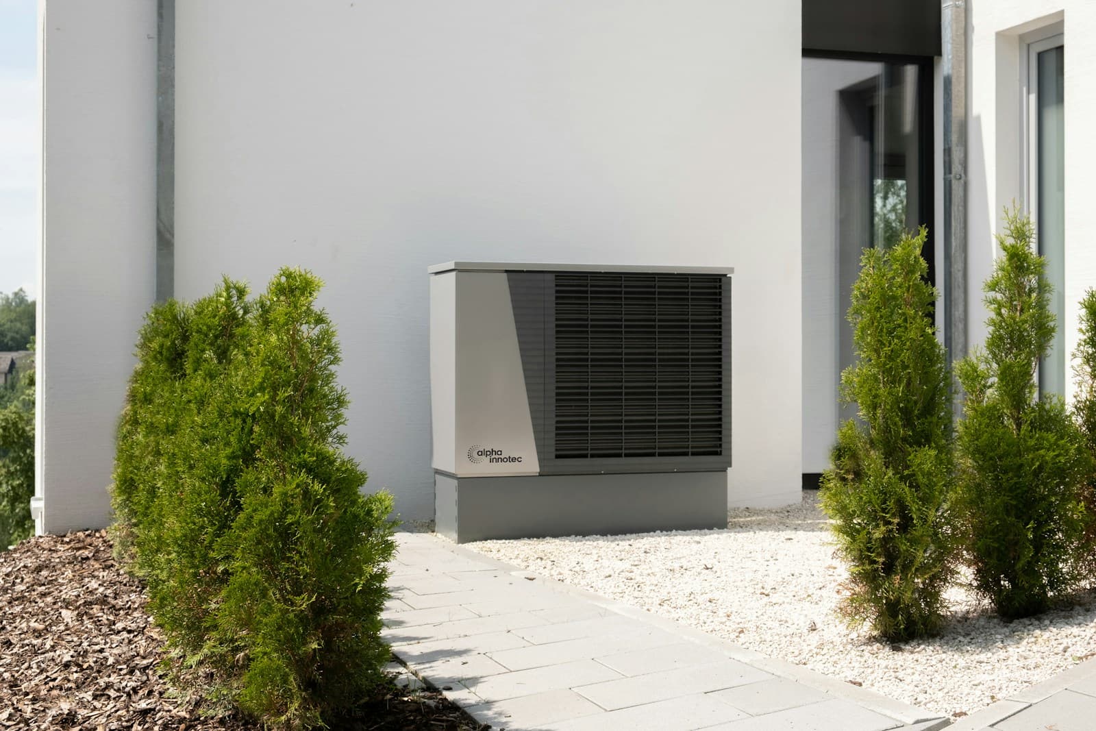 New residential heat pump AC unit installed next to a modern home entryway with landscaped garden