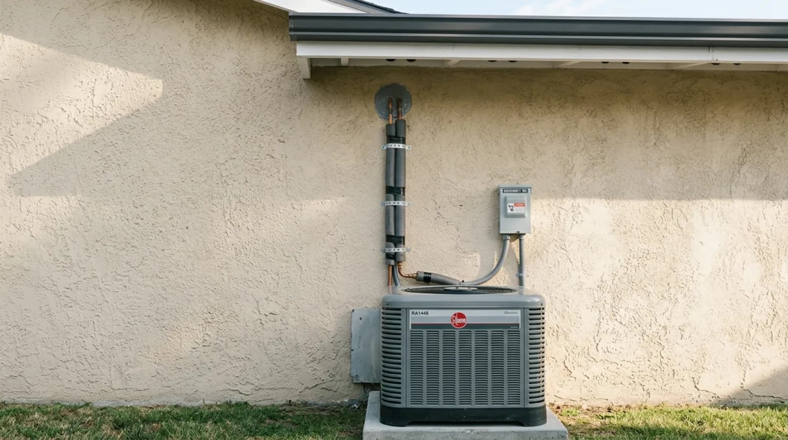 Insulated refrigerant line set strapped to a stucco exterior wall running up into the eave above a new condenser unit