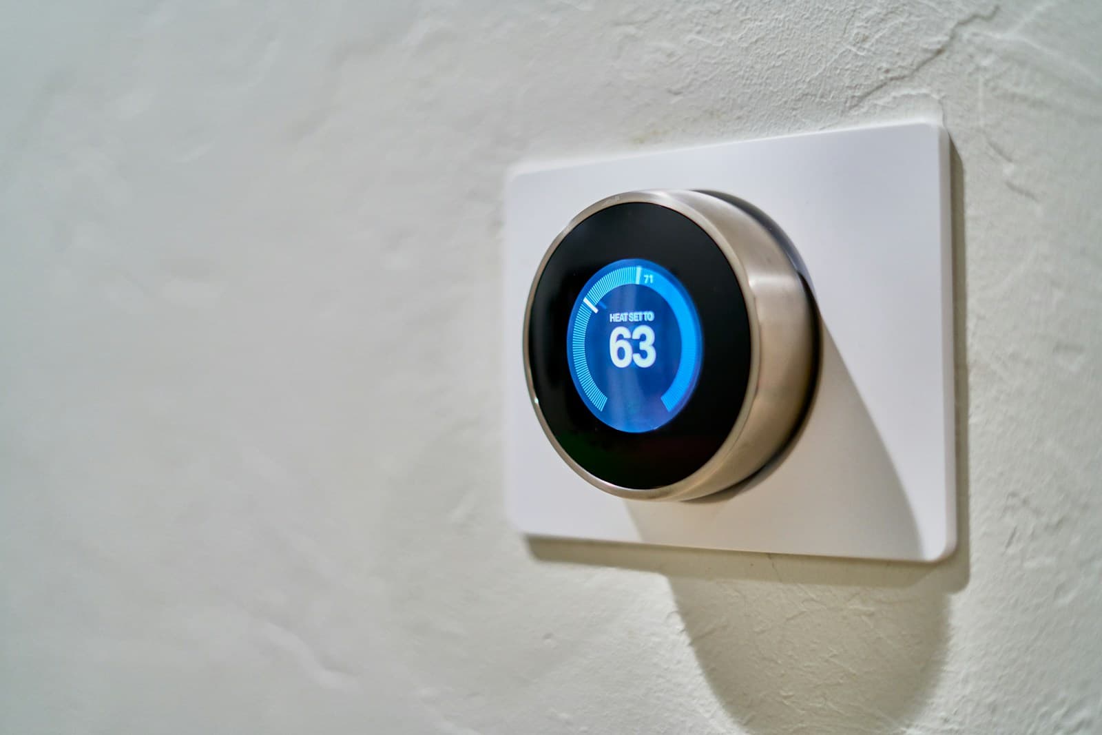 Round Nest-style smart thermostat mounted on a home wall showing heat set to 63 degrees